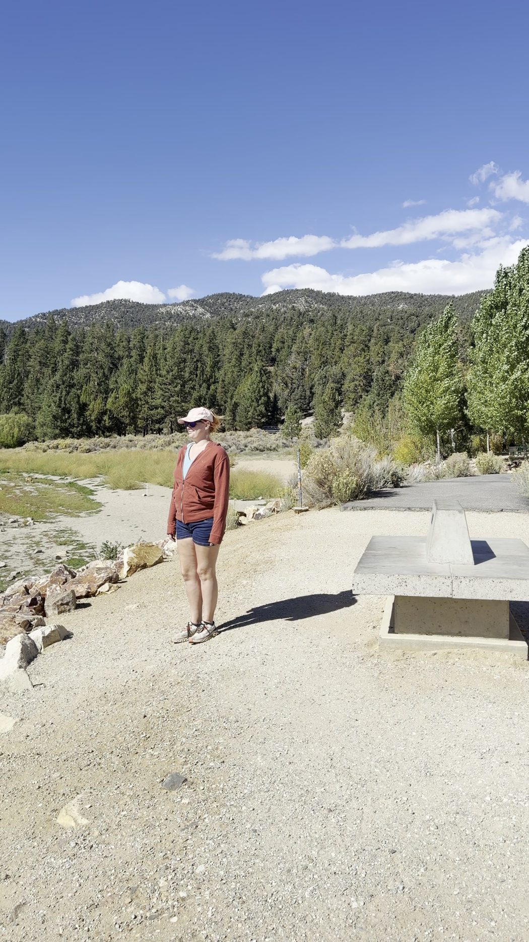 Jenna walking along a gravel path by Big Bear Lake, with pines and mountains behind