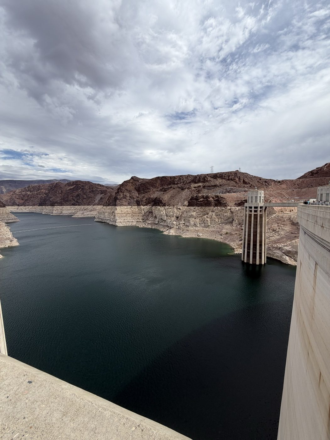 Lake Mead and an intake tower beside the top of Hoover Dam under a cloudy sky