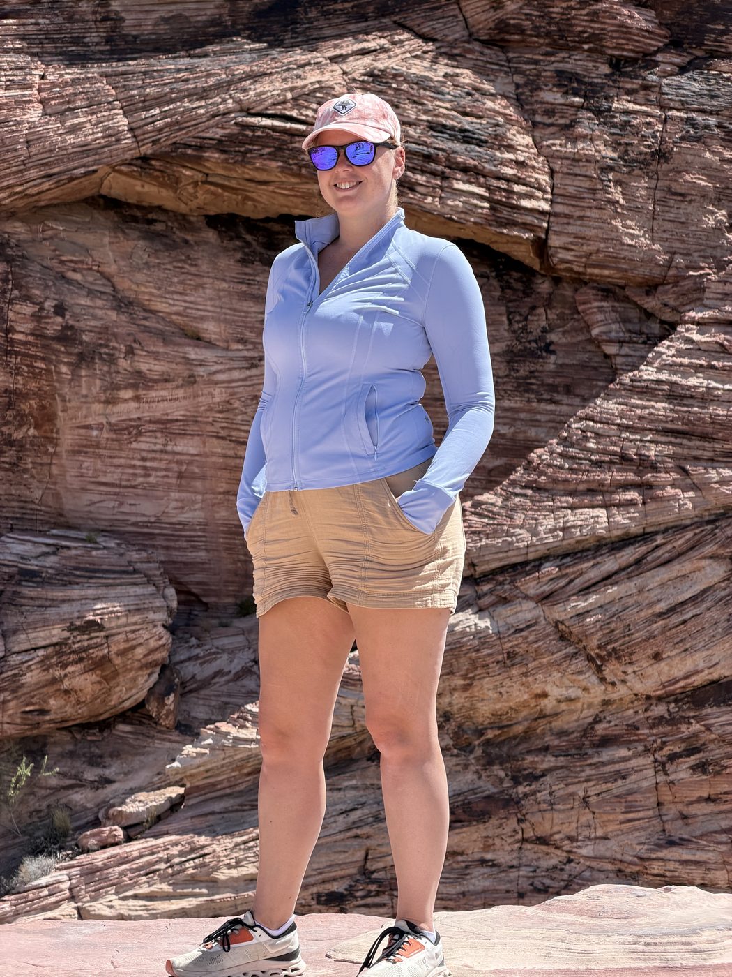 Jenna in a blue zip top and cap standing in front of a wall of red sandstone at Red Rock Canyon