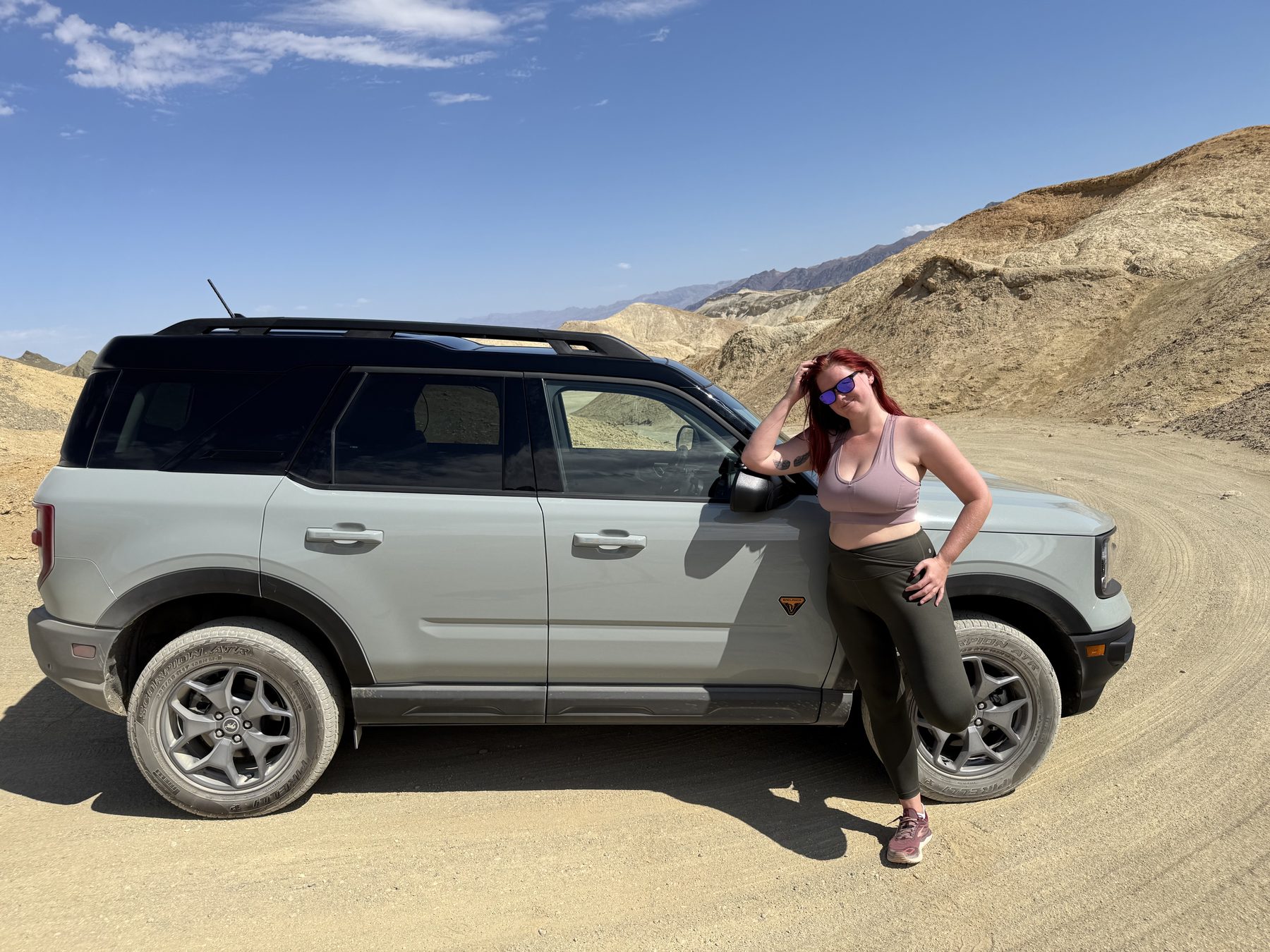 Jenna leaning against Daisy, her Ford Bronco Sport, on a desert road in the Death Valley badlands