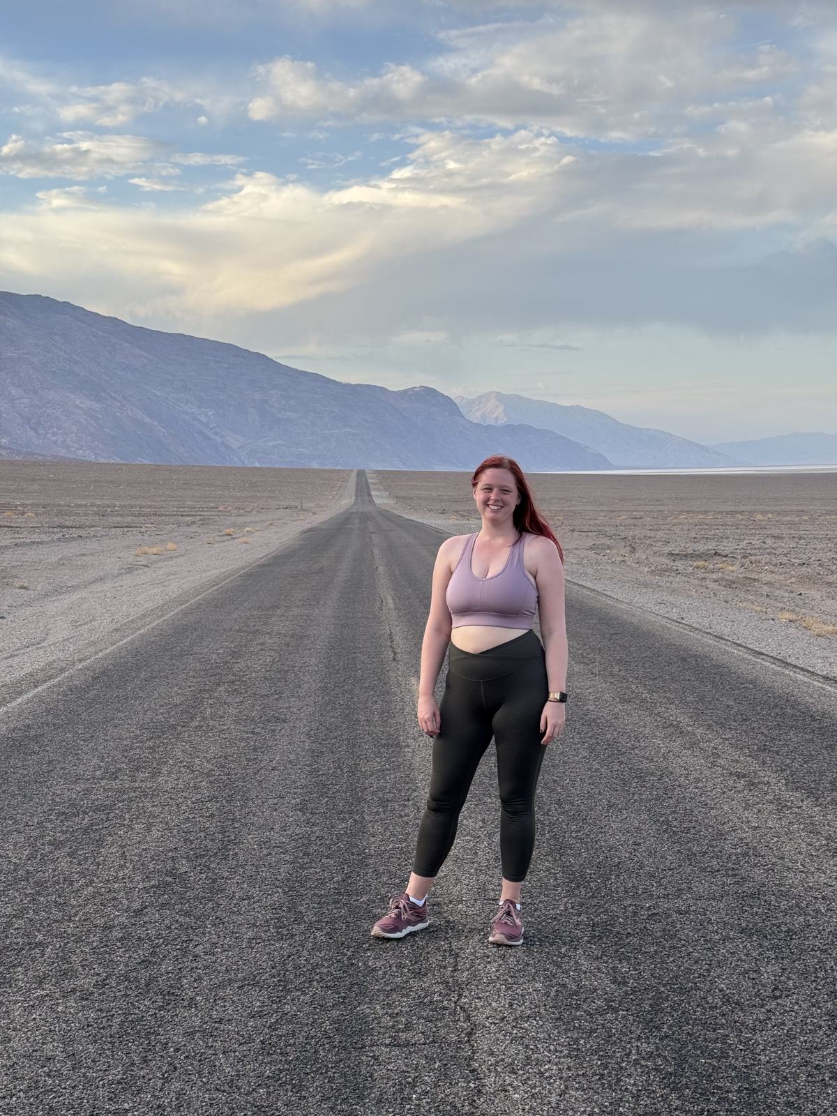 Jenna standing in the middle of an empty desert highway in Death Valley, mountains behind