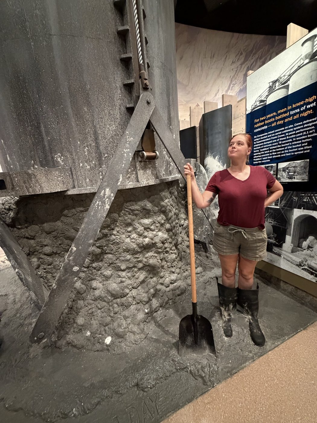 Jenna in wellies holding a shovel in a recreated concrete pour inside the exhibits