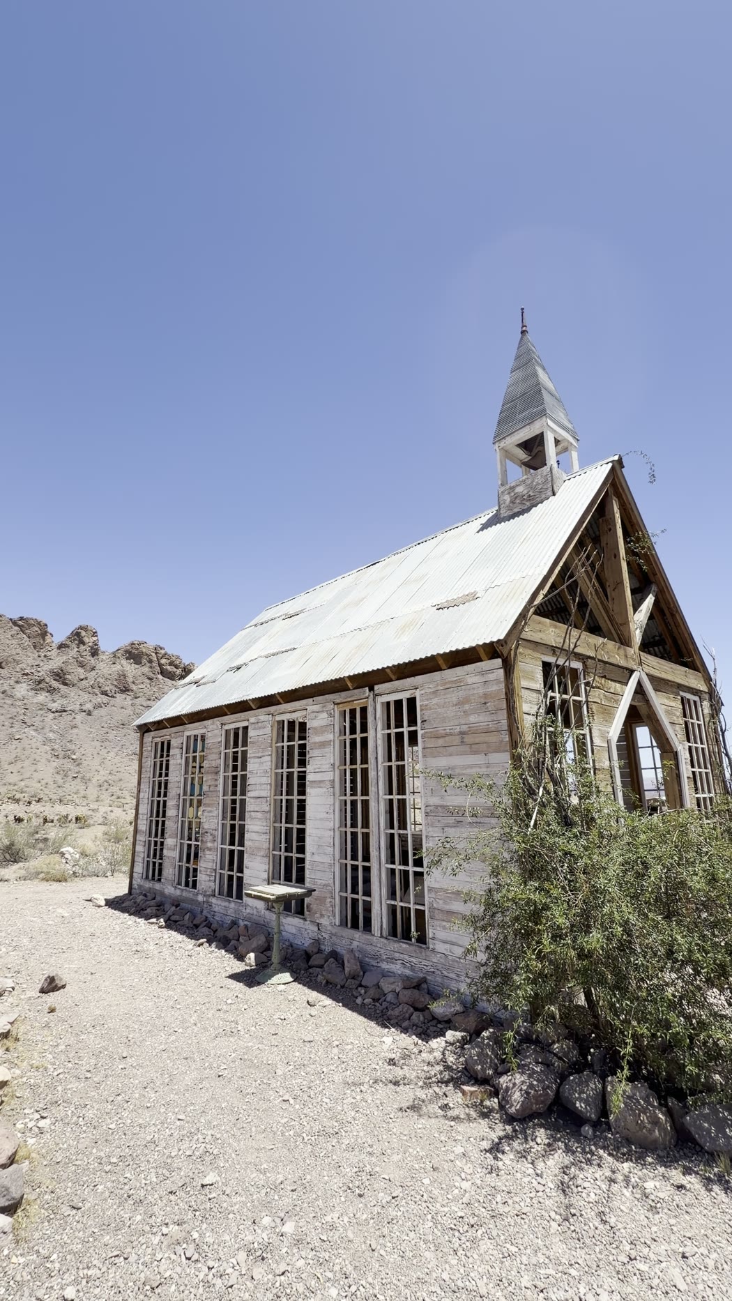 A tidy white wooden chapel with a small steeple and rows of tall windows on gravel