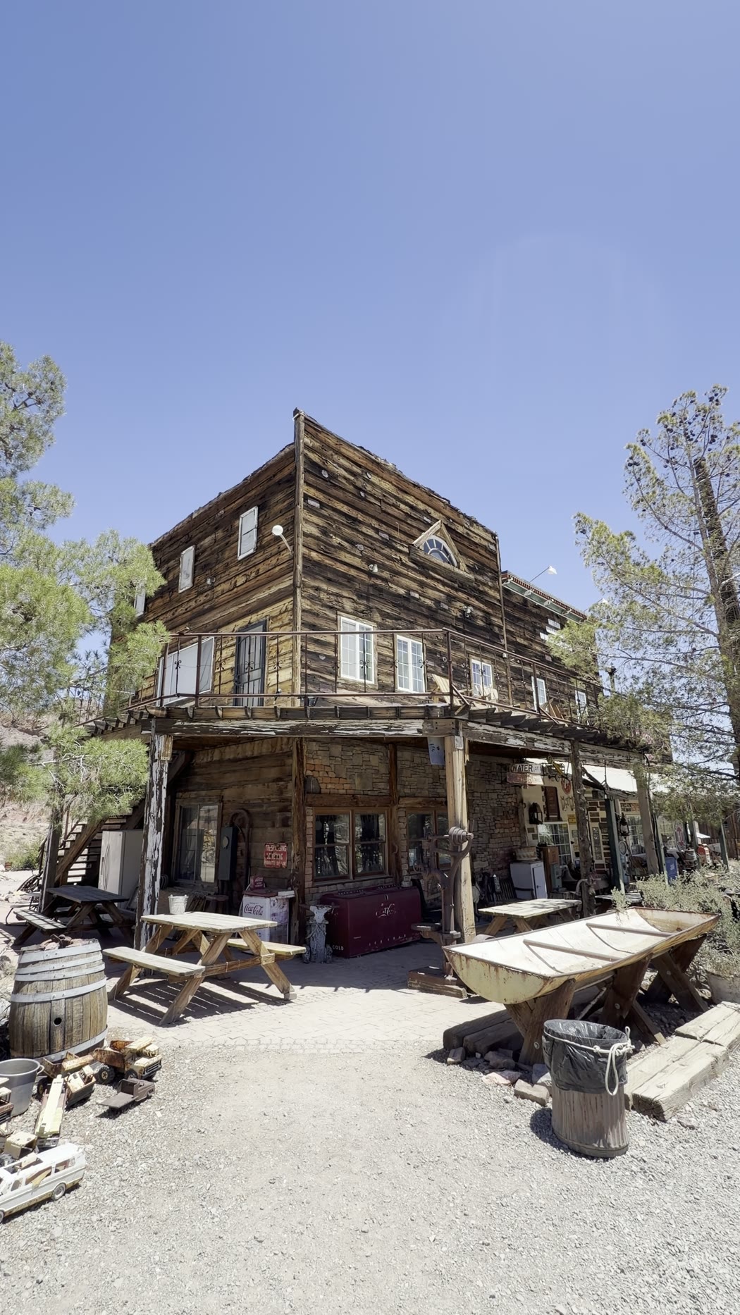 A two-storey weathered wooden building with picnic tables and barrels out front