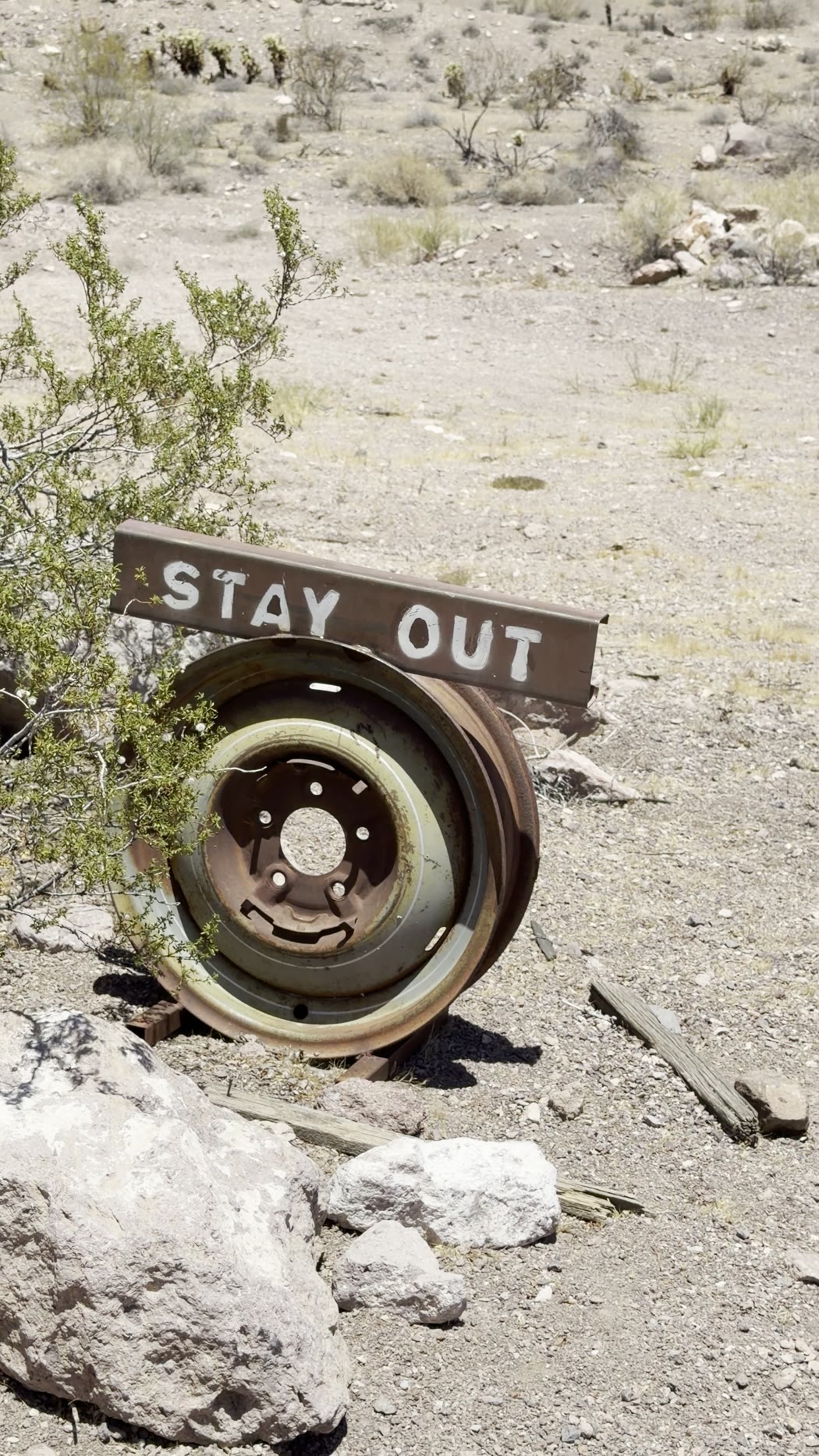 A wooden sign reading STAY OUT propped on an old wheel among desert rocks