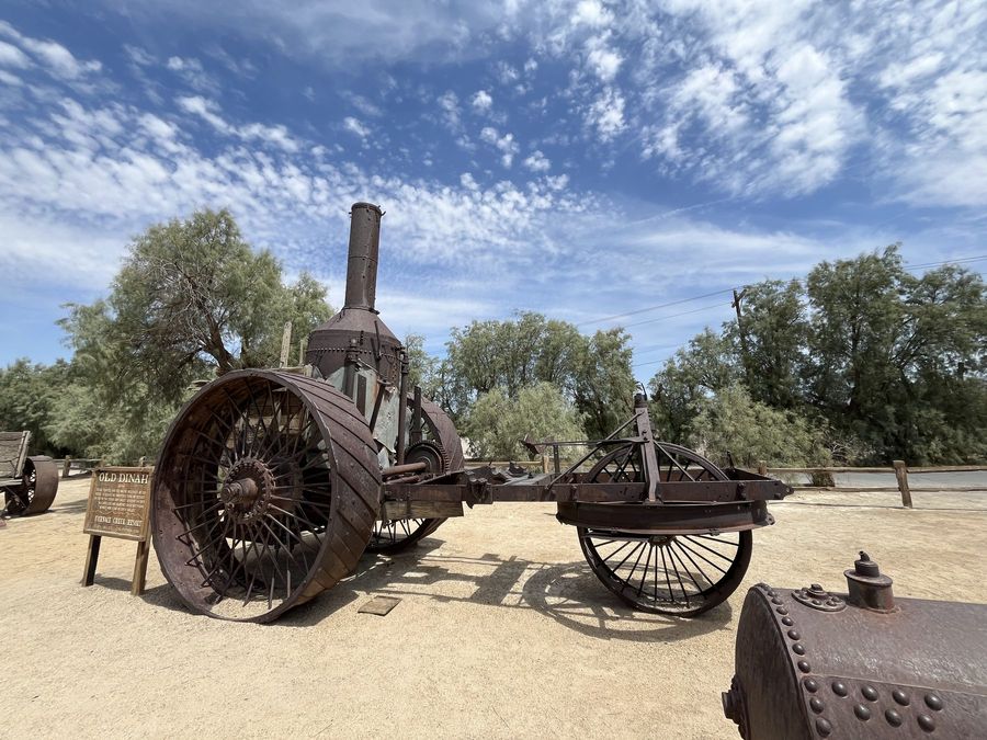 A rusting steam tractor and wagon under a blue sky