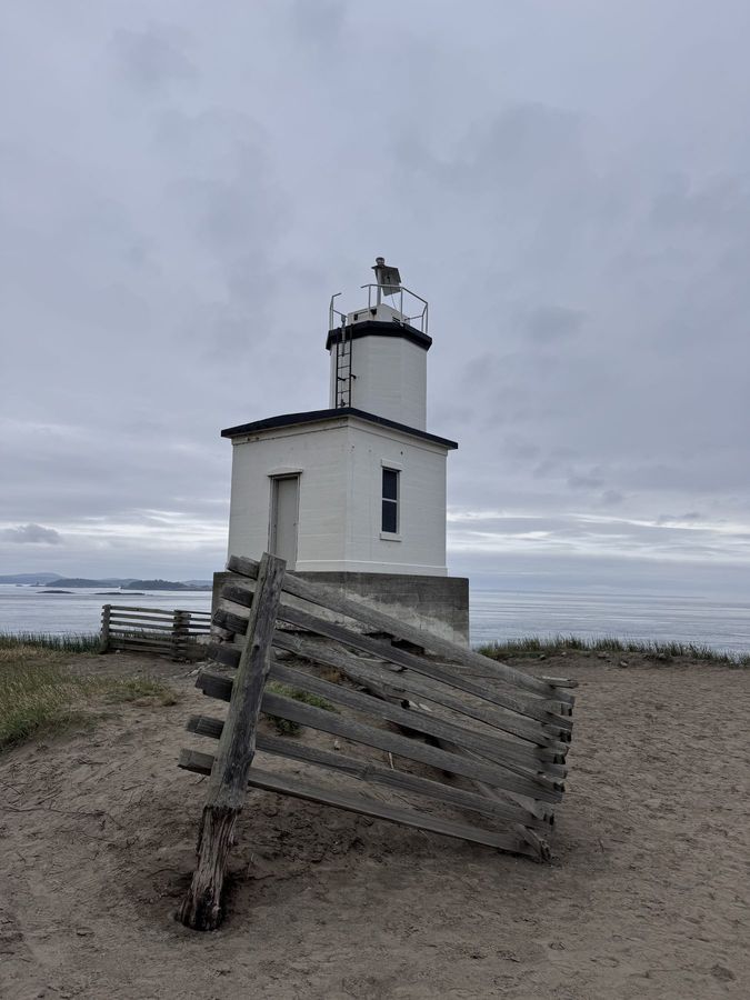 A small white lighthouse on a grassy point