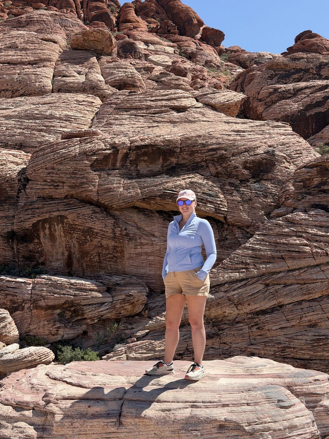 Jenna in a blue zip top and cap standing on layered red and cream sandstone