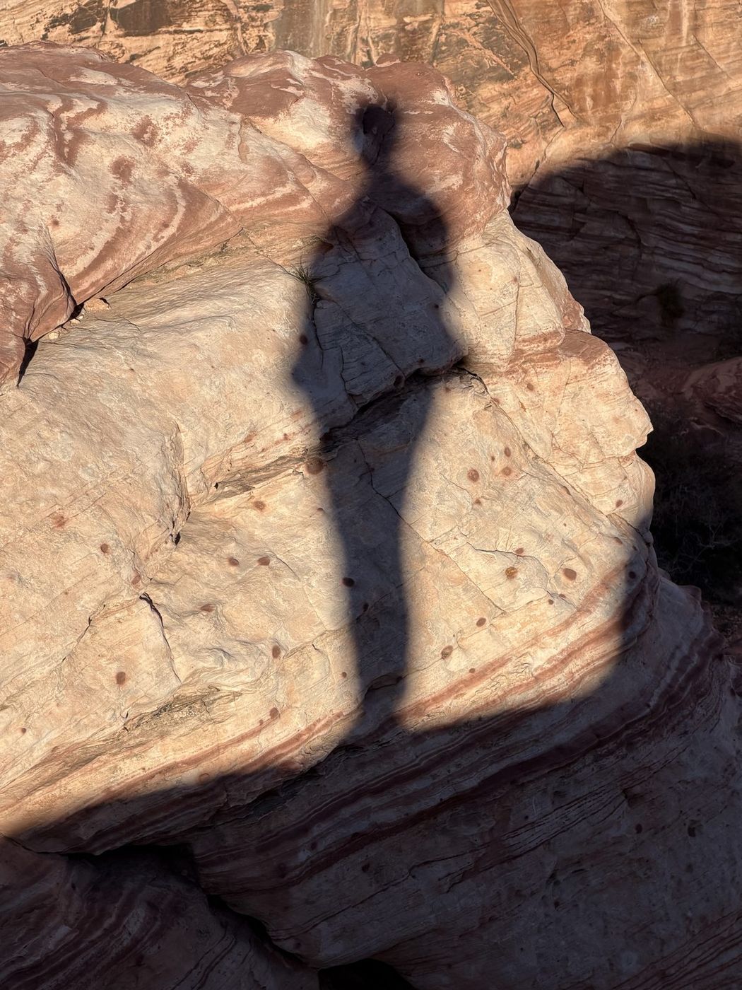 Jenna's long shadow falling across swirled cream and orange sandstone