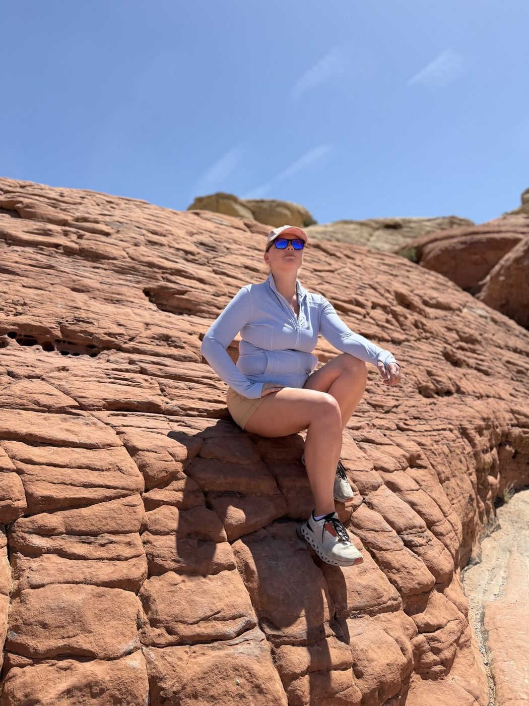 Jenna sitting on a smooth shelf of red sandstone under a clear blue sky