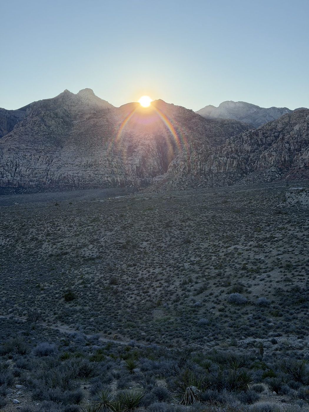 The sun setting behind a mountain range above a wide desert valley