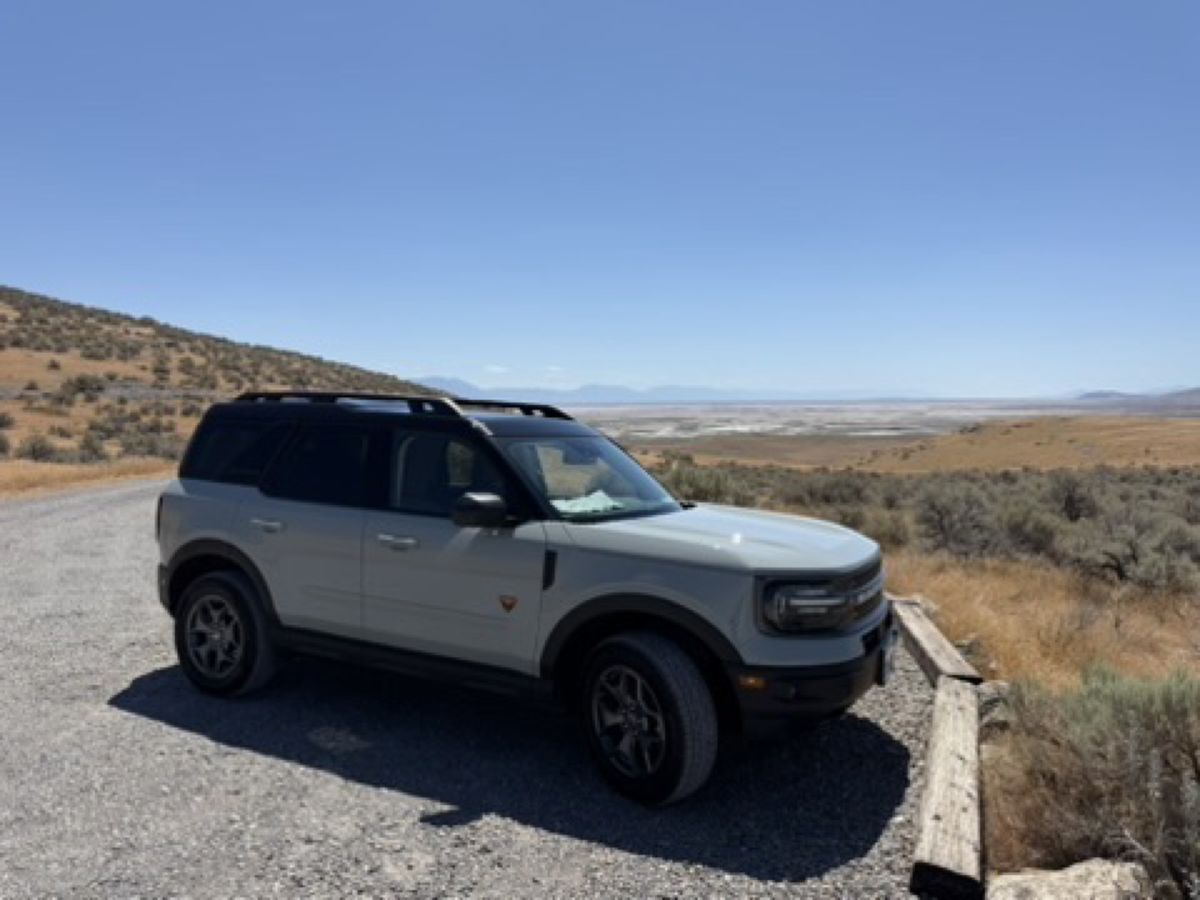 A pale sage Bronco Sport parked at a gravel overlook above a wide dry valley