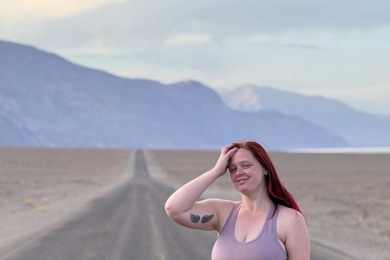 Standing on a long empty desert road with mountains ahead